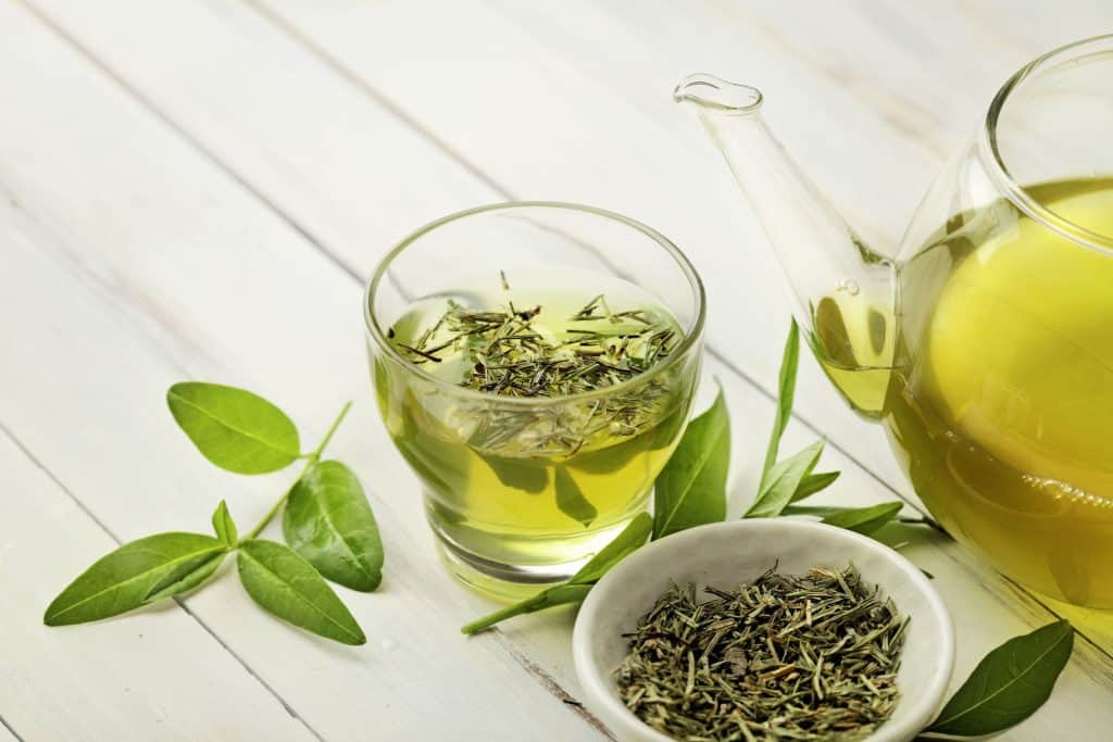 a cup of loose leaf green tea beside a bowl of loose leaves and a tea pot filled with the best green tea for weight loss