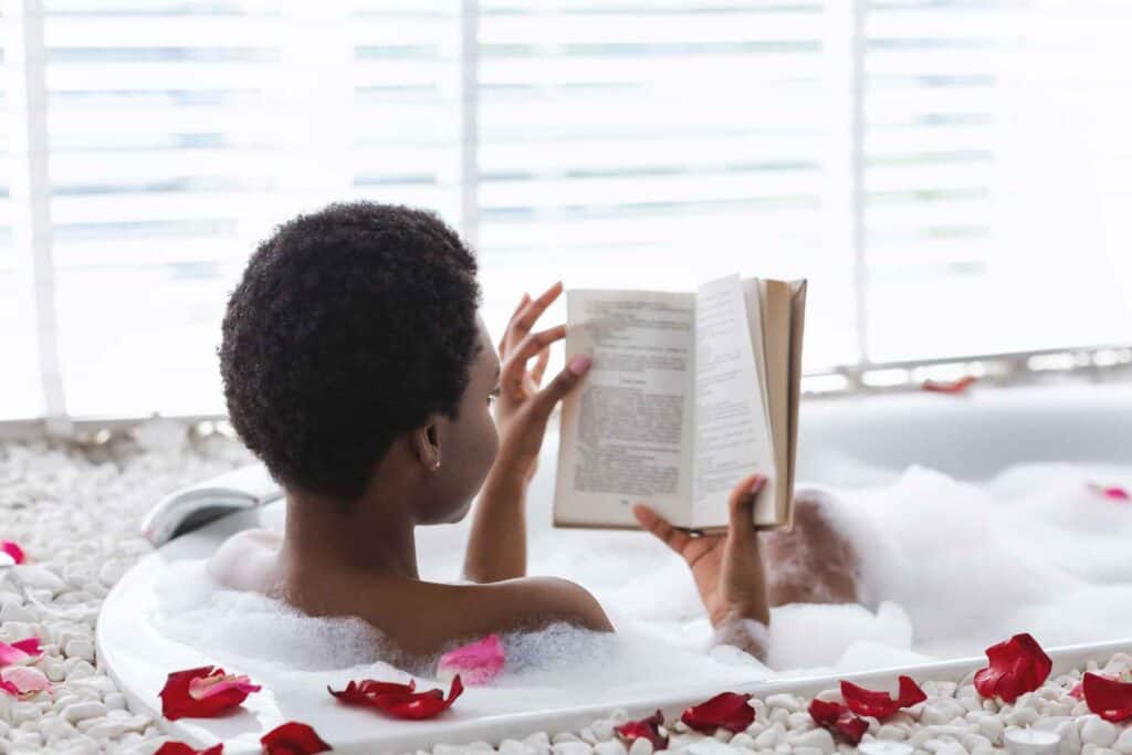 Woman soaking in a bubble bath with rose petals, reading a book. Putting yourself first